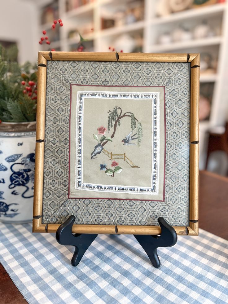 an embroidered picture frame sitting on top of a blue and white checkered table cloth