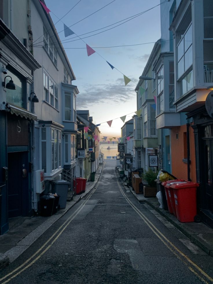 an empty street lined with buildings and flags flying in the air at sunset or dawn