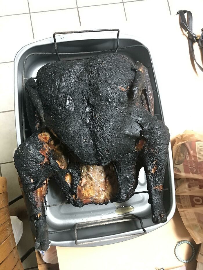 a chicken sitting on top of a metal pan covered in black sauce and burnt to pieces