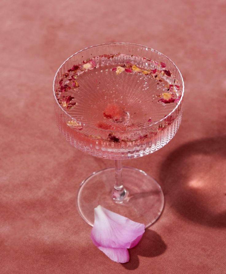 a glass with some flowers in it sitting on a table next to a pink flower