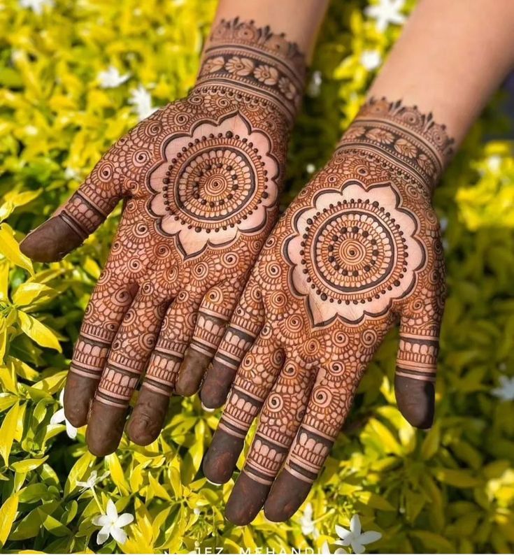 two hands with henna designs on them and some flowers in the foregrounds