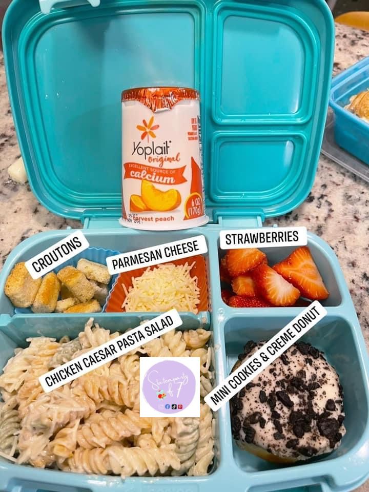 an open lunch box filled with pasta, fruit and yogurt on the side