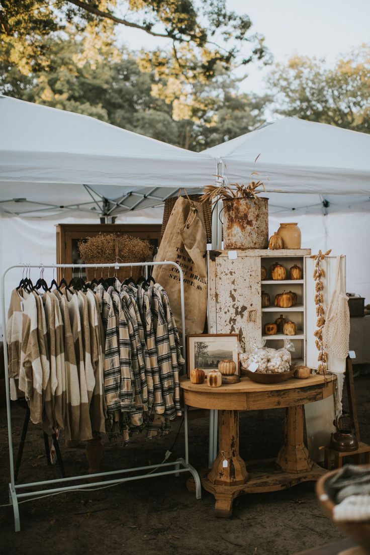 an outdoor market with clothes hanging on racks and other items in front of it under a tent