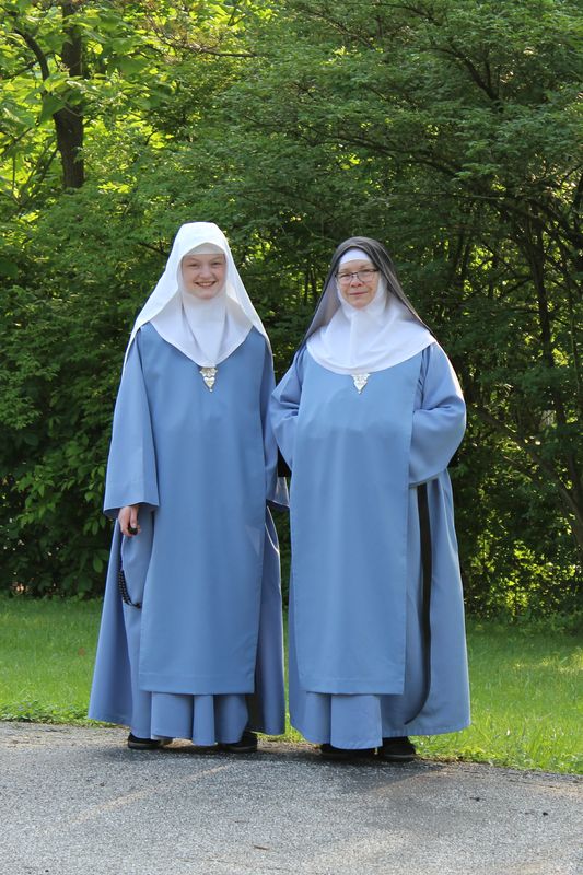 two women dressed in blue robes and white headscarves standing next to each other