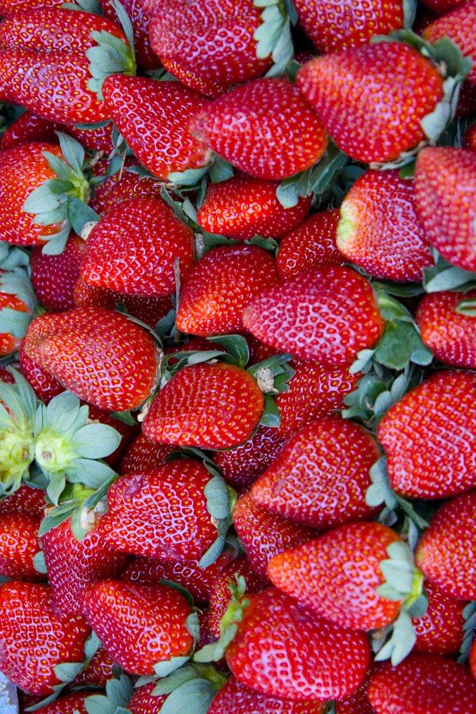 a large pile of red strawberries with green leaves