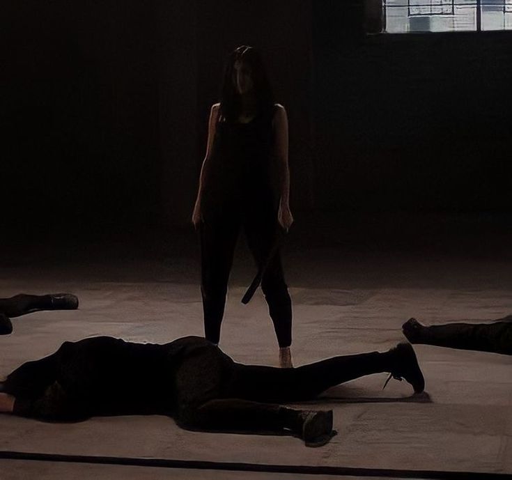 three people are lying on the floor in an empty room, one is holding a knife