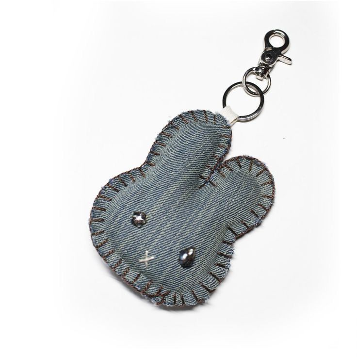 a denim heart shaped keychain hanging from a metal hook on a white background