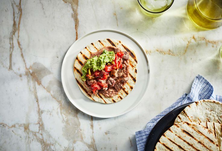 a white plate topped with meat and guacamole next to tortillas