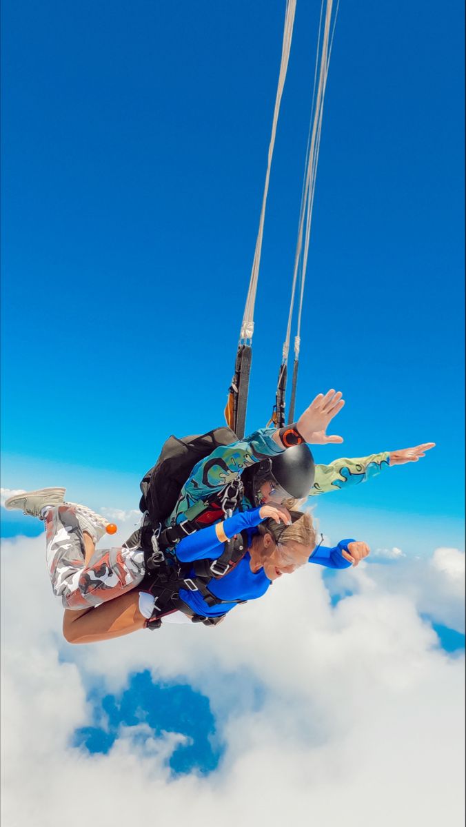 two people in the air with parachutes attached to their backs and feet above clouds