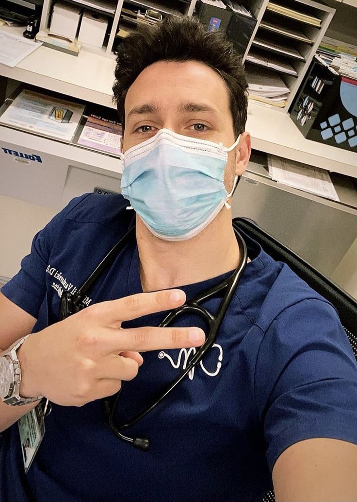 a male doctor wearing a face mask and pointing at the camera