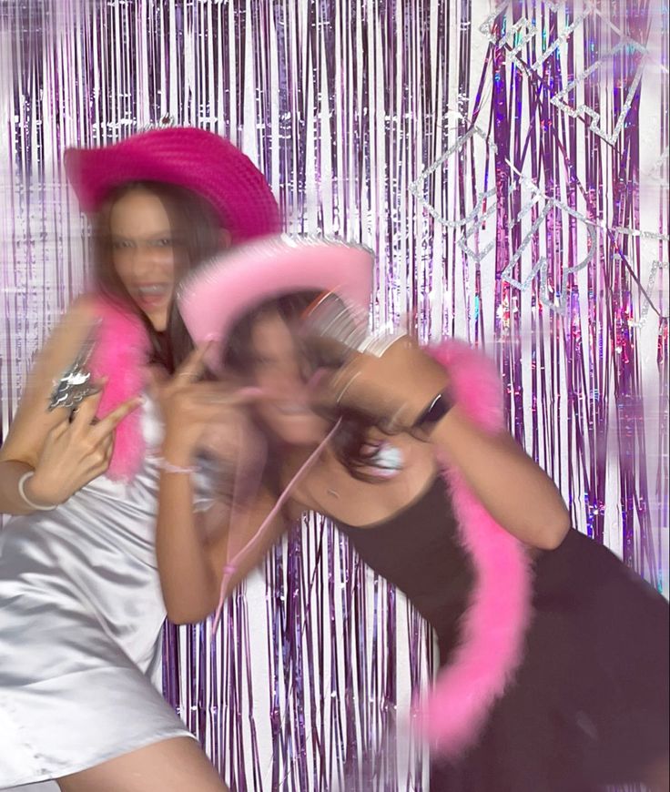 two women are posing for a photo in front of pink tinsel fringes and streamers