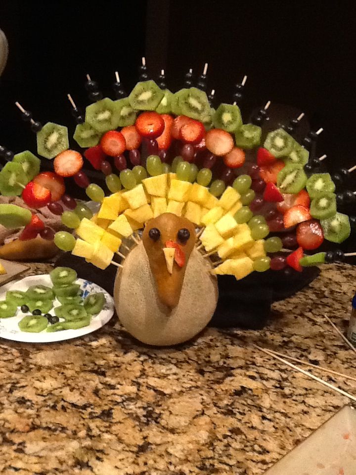 a turkey made out of fruits and vegetables sitting on a counter next to a plate of fruit