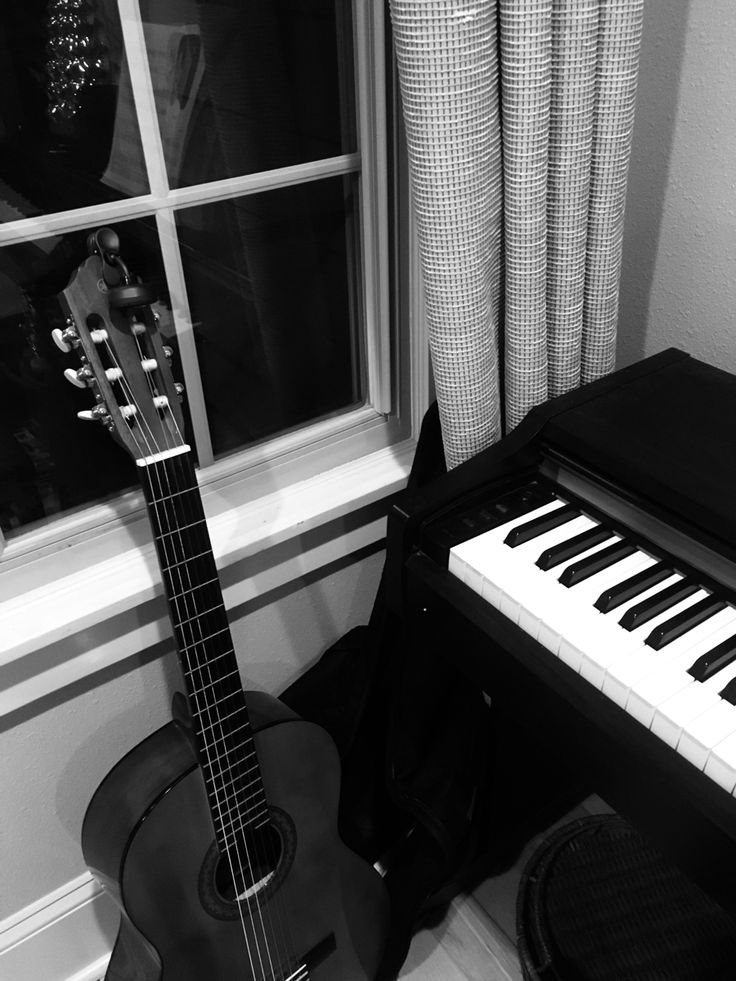 a black and white photo of an acoustic guitar next to a piano keyboard in front of a window