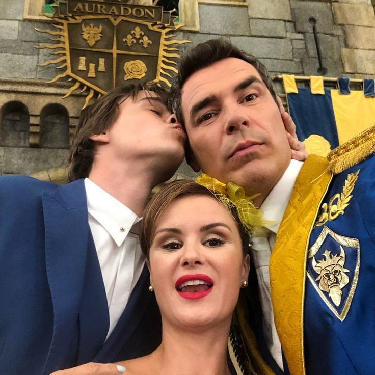 two men and a woman posing for a photo in front of a castle with their arms around each other