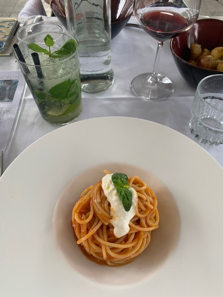 a white plate topped with pasta and sauce next to glasses of wine on a table