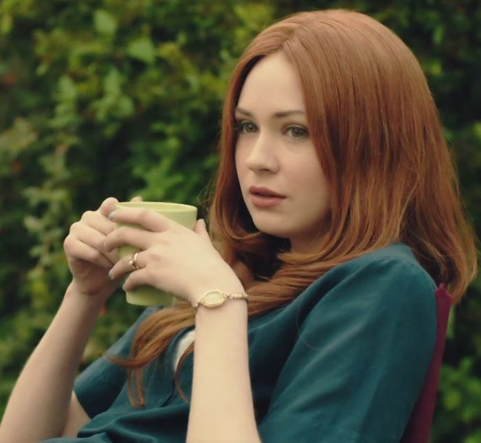 a woman with red hair is holding a cup in her hand and looking off into the distance