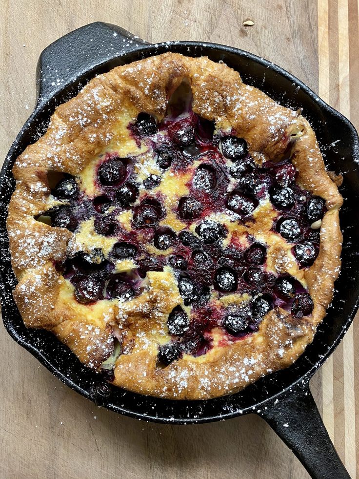 a blueberry pie in a cast iron skillet on a wooden table with powdered sugar