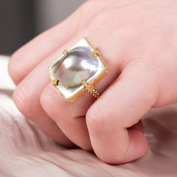 This natural Mabe Pearl is in the shape of a square. It seems to burst out of its golden frame, giving it a 3D quality. We highlighted the natural beauty of this one-of-a-kind gemstone by encasing it in a handmade, 18k gold bezel.Ready to ship in size 7. Please allow 1-2 weeks for any other size. Technical Details Metal: 18k yellow goldMabe Pearl: 18.42 cts.Ring face: 22 x 22mmBand width: 2mmHandmade in New YorkStyle # R-2467-MP Elegant Gold Square Rings, Elegant Square Gold Ring, Gold Rectangular Cabochon Rings, Rectangular Gold Cabochon Rings, Rectangular Cabochon Gold Rings, Yellow Gold Rectangular Bezel Set Jewelry, Rectangular Yellow Gold Jewelry With Bezel Setting, Rectangular Bezel-set Yellow Gold Jewelry, Elegant Square Yellow Gold Jewelry