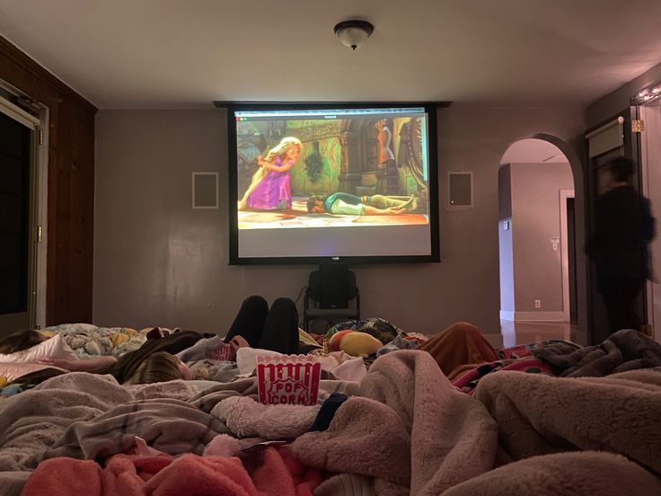 a person watching a movie on the screen in a room with many blankets and pillows