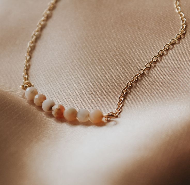 Seeking solace in the gentle embrace of pink opals? Our Pink Opal Curved Necklace is a beacon of emotional healing and tranquility.Crafted with delicate care, this necklace features seven 2mm pink opal gemstones delicately arranged in a graceful curve, symbolizing the soothing path to inner peace. The necklace is available in your choice of sterling silver or gold-filled.Adorned on a chain adjustable from 16 to 18 inches, this necklace offers versatility, ensuring a perfect fit for any occasion. Whether worn close to the heart or draped elegantly around the neckline, its presence is sure to evoke feelings of comfort and calmness.Features:- Seven 2mm pink opal gemstones- Curved design for a unique touch- Available in sterling silver or gold-filled- Adjustable chain length (16 to 18 inches) Pink Opal Round Beads Necklace For Gift, Dainty Gold Pink Opal Jewelry, Dainty Pink Opal Gold Jewelry, Adjustable Gold Jewelry With Pink Opal, Adjustable Gold Pink Opal Jewelry, Adjustable Pink Opal Gold Jewelry, Delicate Pink Opal Jewelry Gift, Gold Pink Opal Necklace For Gifting, Gold Pink Opal Necklace For Gift