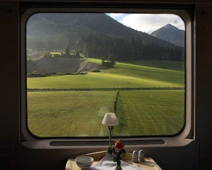 a table with a lamp on it in front of a window overlooking a green field