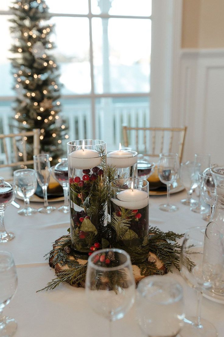 a centerpiece with candles and greenery on a table in front of a christmas tree