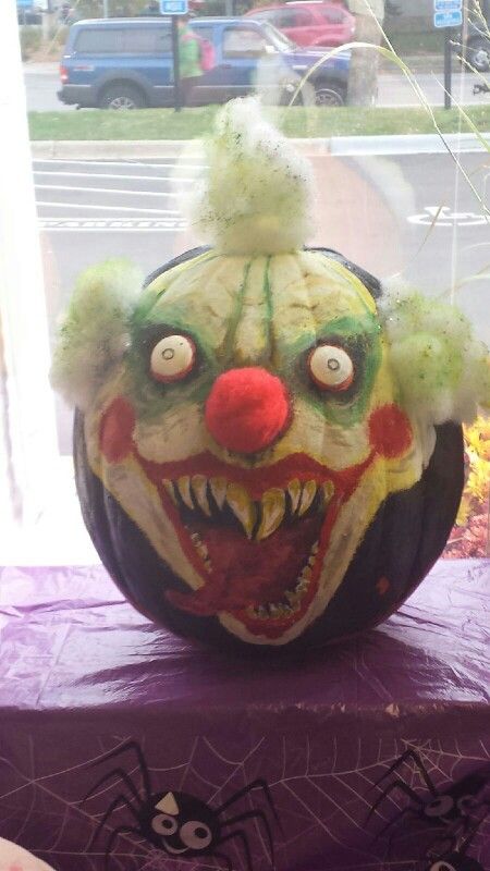 a carved pumpkin with an evil clown's face on it, sitting in front of a window