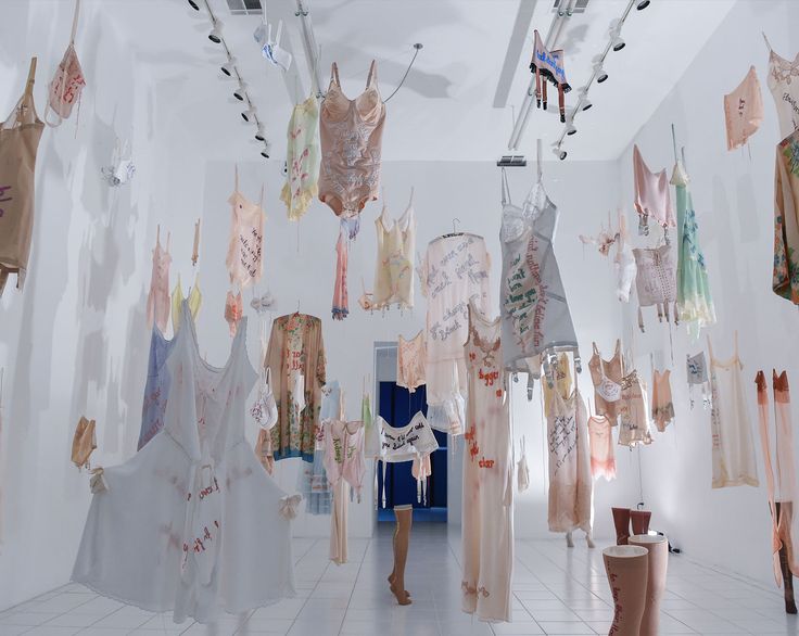 there are many clothes hanging from the ceiling in this room, and one person is walking down the hall