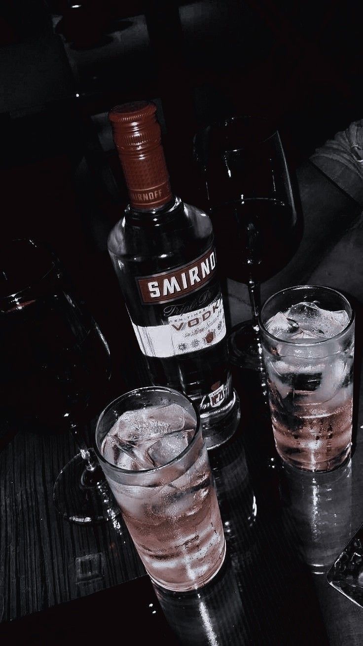 two glasses filled with ice sitting next to a bottle