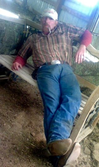 a man laying down on a bench in the middle of some dirt and hay covered ground