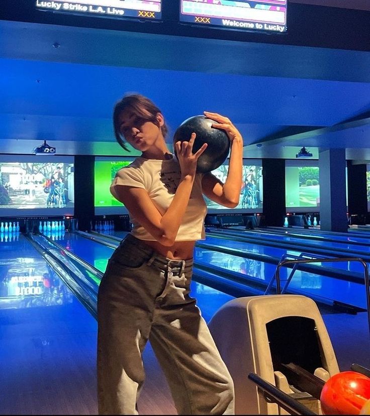 a woman holding a bowling ball in her right hand while standing next to some bowling lanes