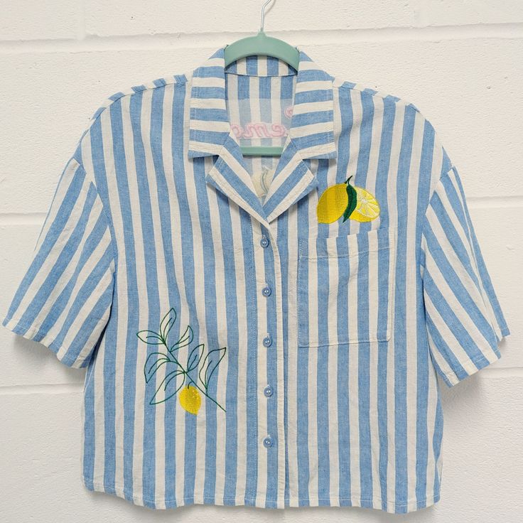 Cropped oversized linen shirt, great for those hot and sunny summer days. Pale blue and white soft linen and viscose shirt with embroidered lemons on the front and back. Text on the reverse reads 'Lemon Squeezy' in pink embroidered lettering. These are good quality hardly warn second hand shirt which I have embroidered and refashioned. They are oversized in style and there are 3 available in different sizes.  Please check your size below: Original garment size - Woman's UK 8 Material - 55% Linen 45% Viscose Measurements - Armpit to armpit (laying flat): 51cm Length (collar to hem): 54cm Sleeve: Short 22cm from shoulder seam Original garment size - Woman's UK 10 Material - 55% Linen 45% Viscose Measurements - Armpit to armpit (laying flat): 53cm Length (collar to hem): 54cm Sleeve: Short 22 Summer Embroidered Collared Tops, Summer Embroidered Relaxed Fit Shirt, Summer Vacation Tops With Lemon Print, Embroidered Relaxed Fit Shirt For Summer, Spring Embroidered Linen Shirt, Summer Collared Tops With Floral Embroidery, Collared Tops With Floral Embroidery For Vacation, Embroidered Cotton Shirt For Vacation, Casual Shirt With Floral Embroidery For Vacation