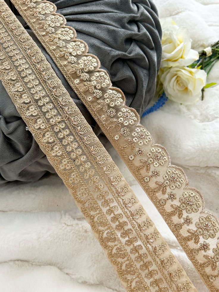 three gold lace trims sitting on top of a pile of white flowers next to a gray pillow