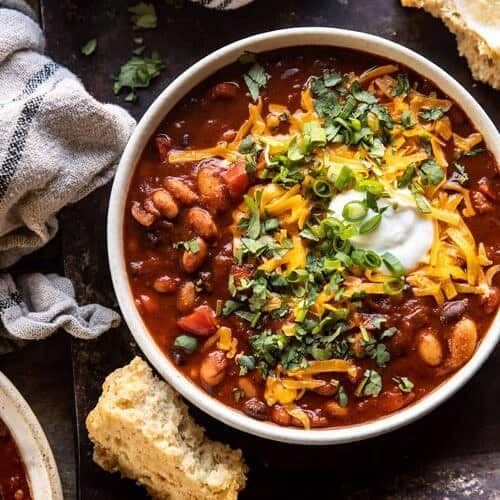 a white bowl filled with chili and beans next to some bread on a wooden table