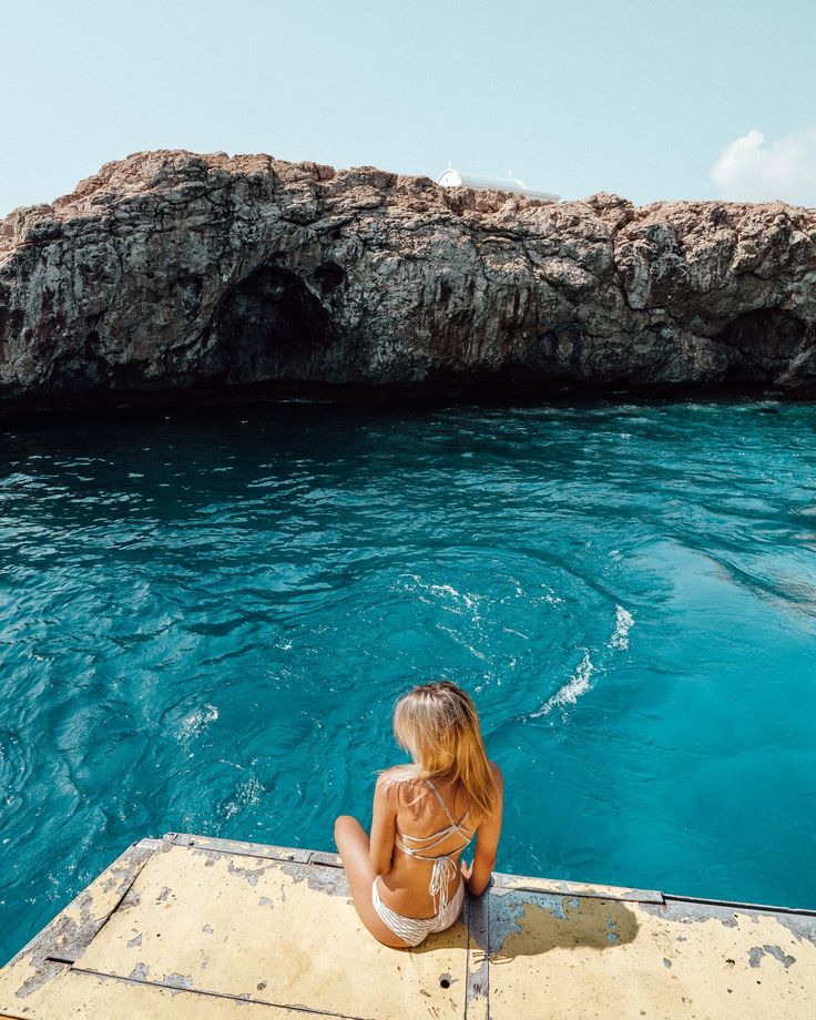 a woman sitting on the edge of a boat looking out at the water and rocks