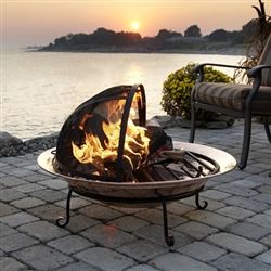 a fire pit sitting on top of a brick patio next to the ocean at sunset