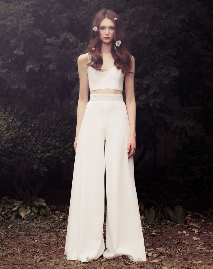 a woman standing in front of trees wearing white pants and cropped top with cutouts