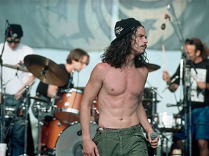 a shirtless man with long hair and no shirt on standing in front of a band