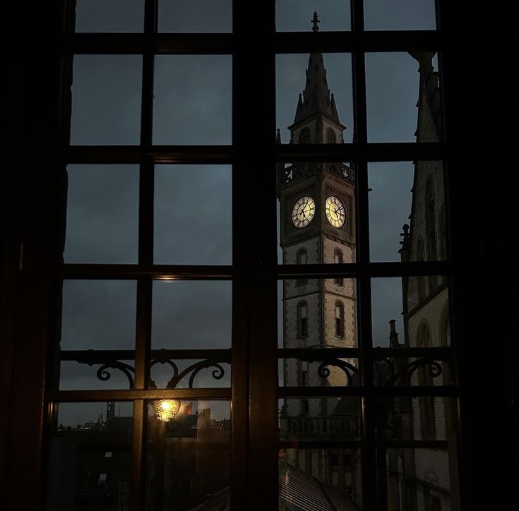 a clock tower seen through a window at night