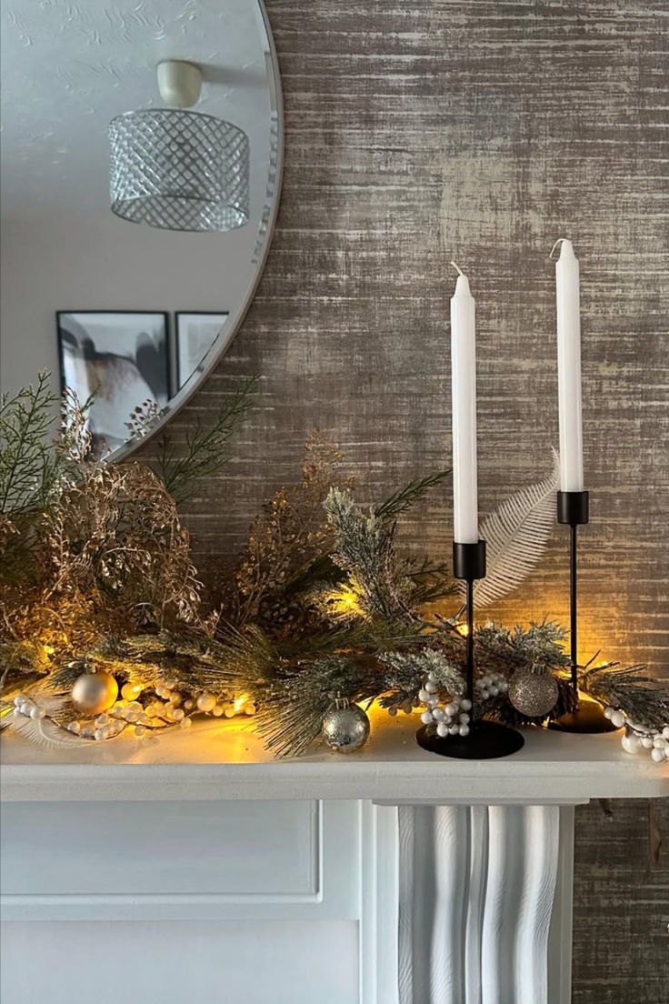 two candles are sitting on top of a mantle with greenery and lights around it