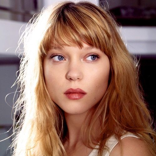 a woman with long blonde hair and blue eyes posing for a photo in a white tank top