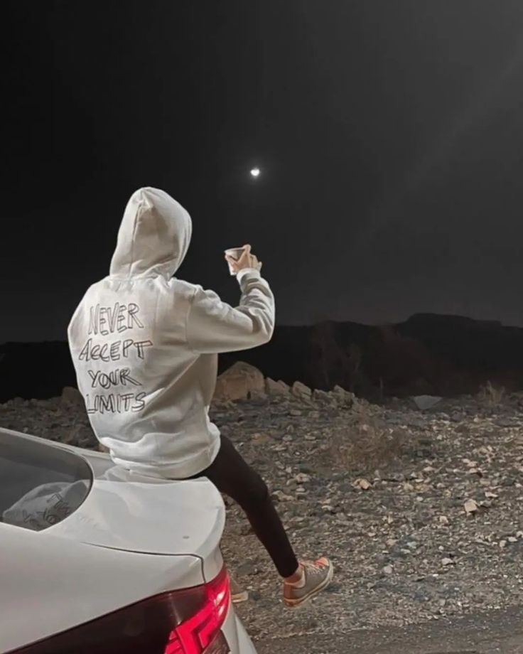 a person sitting on the hood of a car and holding something up to their face