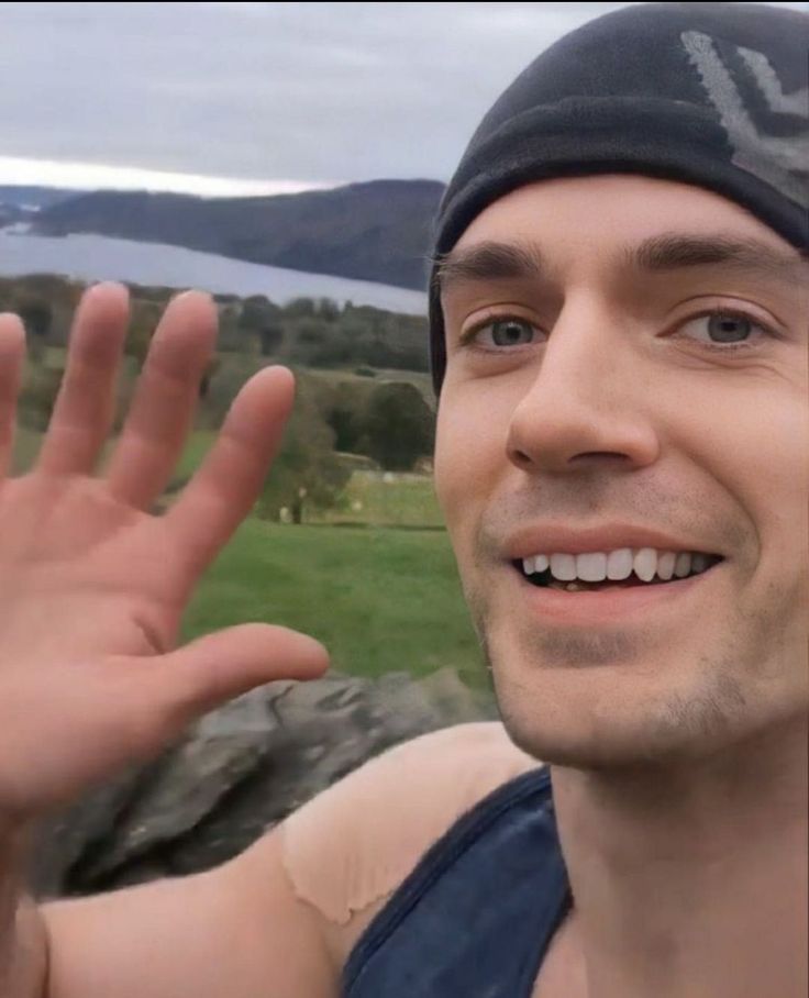 a man wearing a beanie is waving at the camera with his hand in front of him