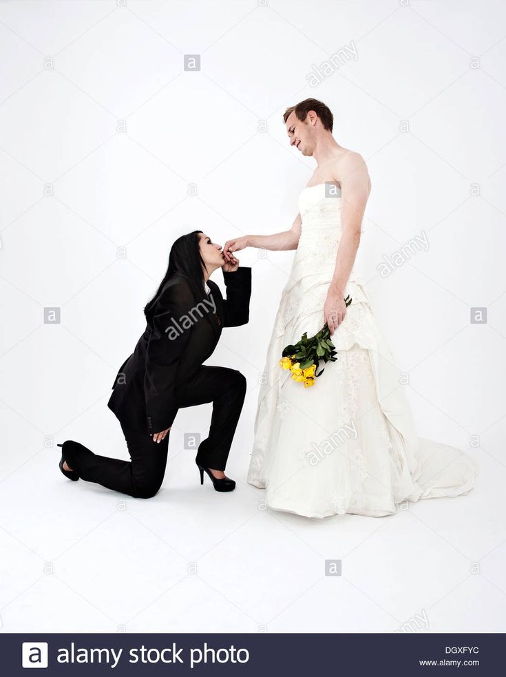 a bride and groom kneeling down to each other in front of a white background - stock image