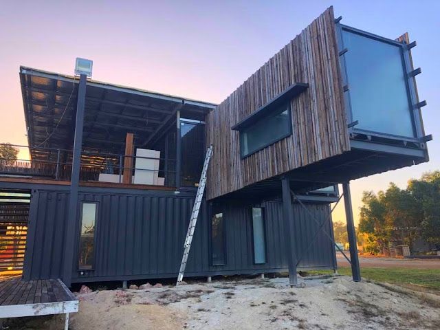 two shipping containers are stacked on top of each other in front of a house that has been built into the ground