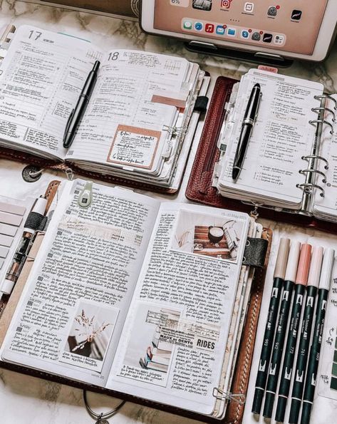 several notebooks and pens are spread out in front of an open laptop on a table