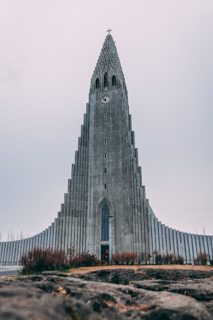 a very tall building with a clock on it's face in front of some rocks