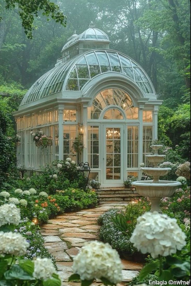 a glass house surrounded by white flowers and greenery in the middle of a forest