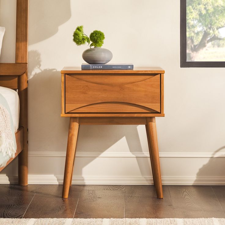 a small wooden table with a potted plant sitting on it's top next to a bed