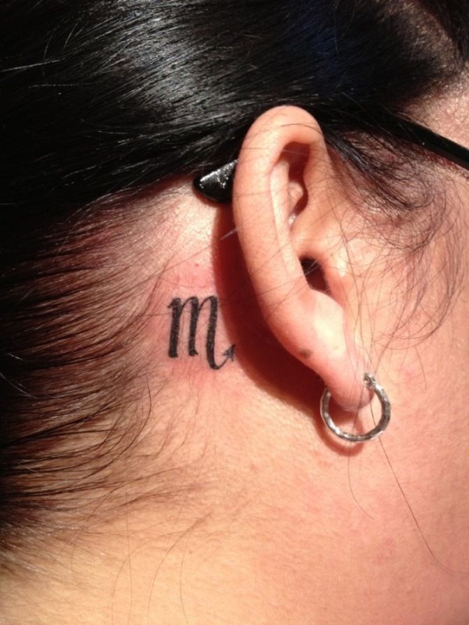 a woman's ear with the word mom tattooed on her left behind the ear